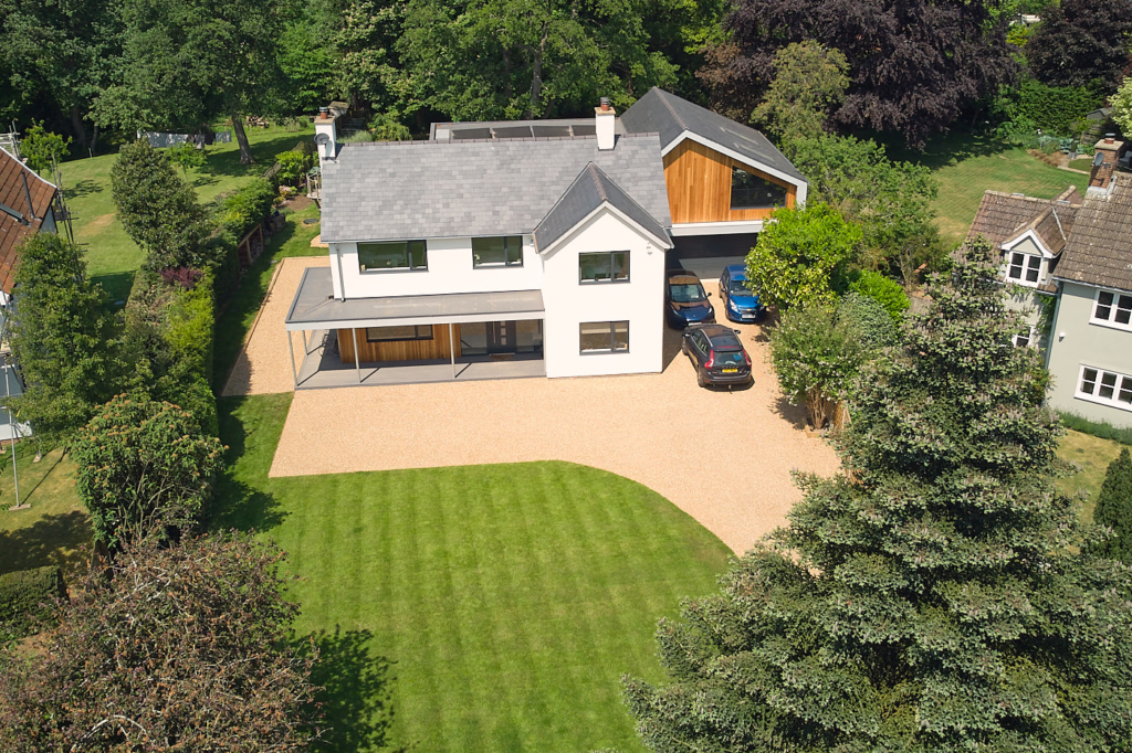 Aerial view of the house, front garden and drive with mature trees in the background.